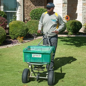 Technician using a spreader to apply lawn treatment in a San Antonio, TX yard