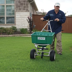 Technician using a spreader to apply lawn treatment in a Round Rock, TX yard